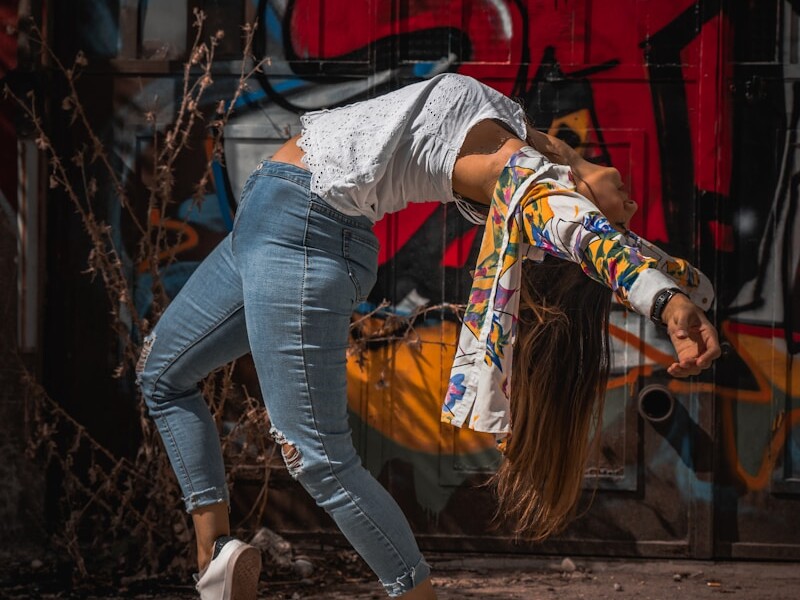 woman in blue denim jeans and white long sleeve shirt standing near red wall